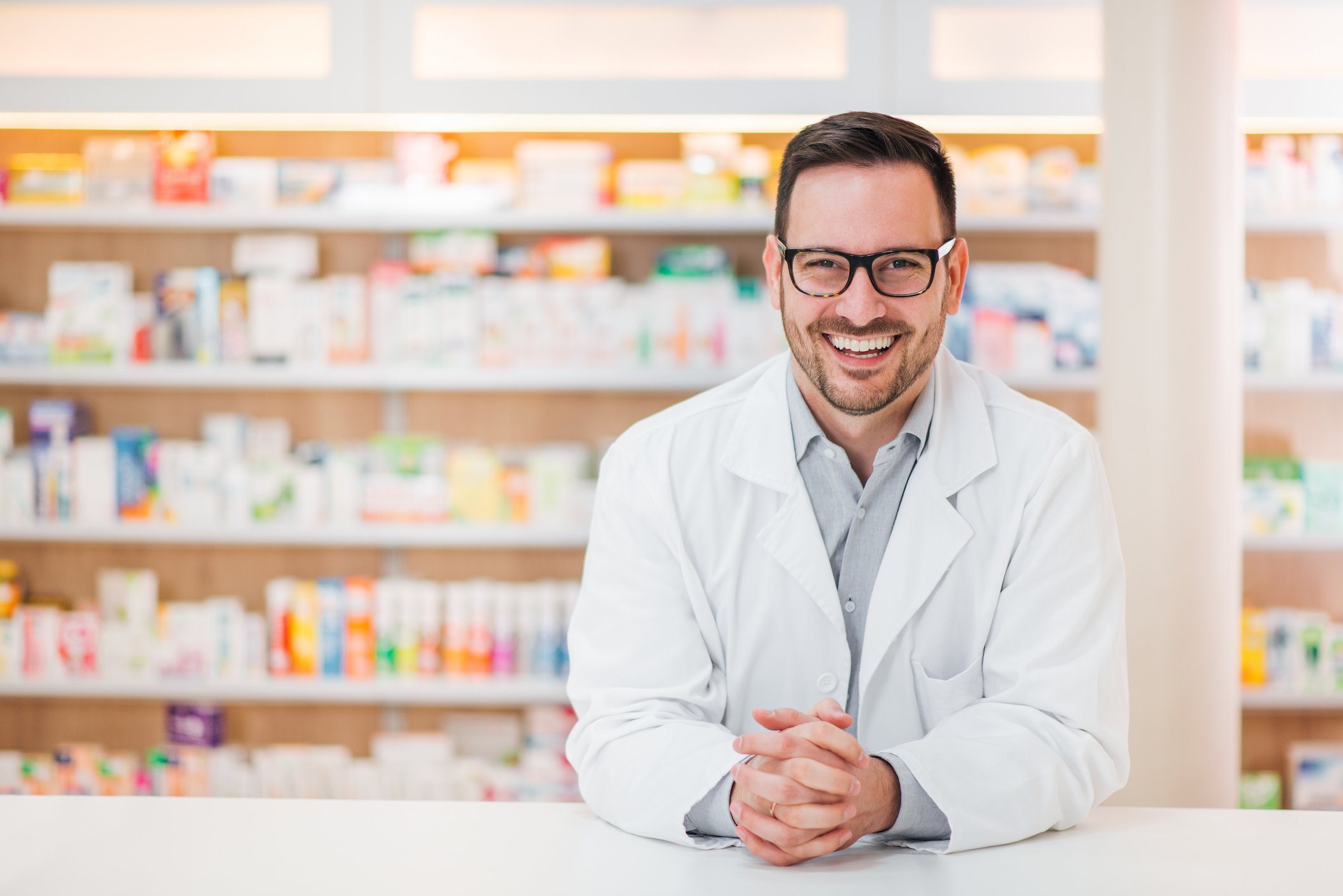 Smiling pharmacist leaning on a countertop inside a pharmacy.