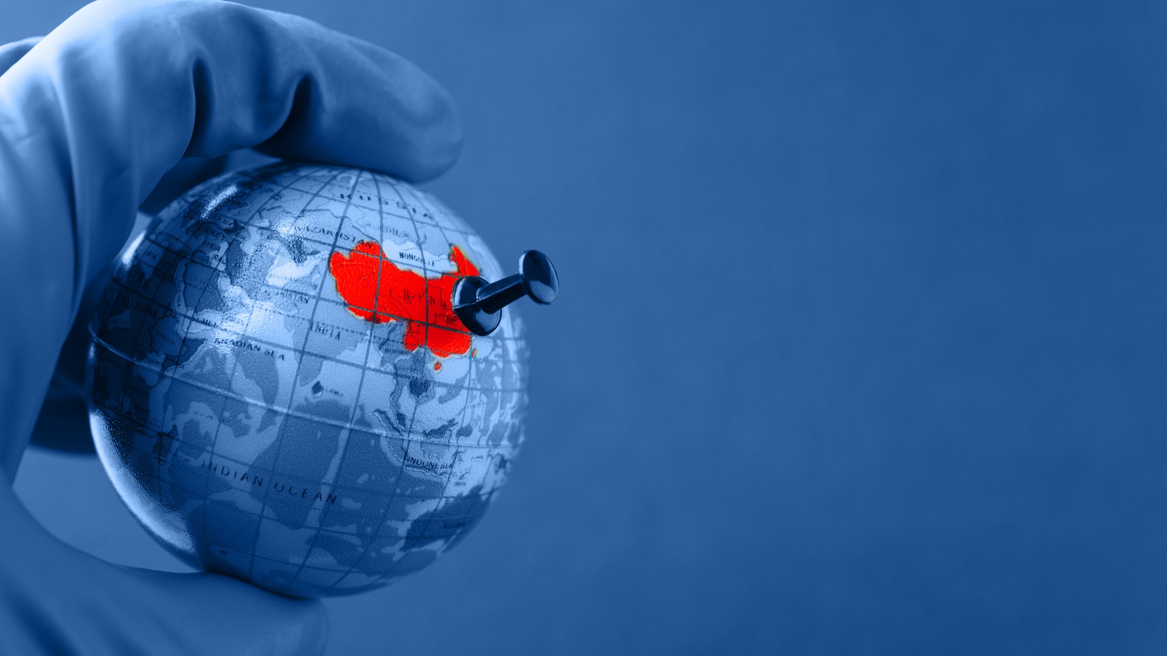 Gloved hand holding a tiny globe with a pushpin in China