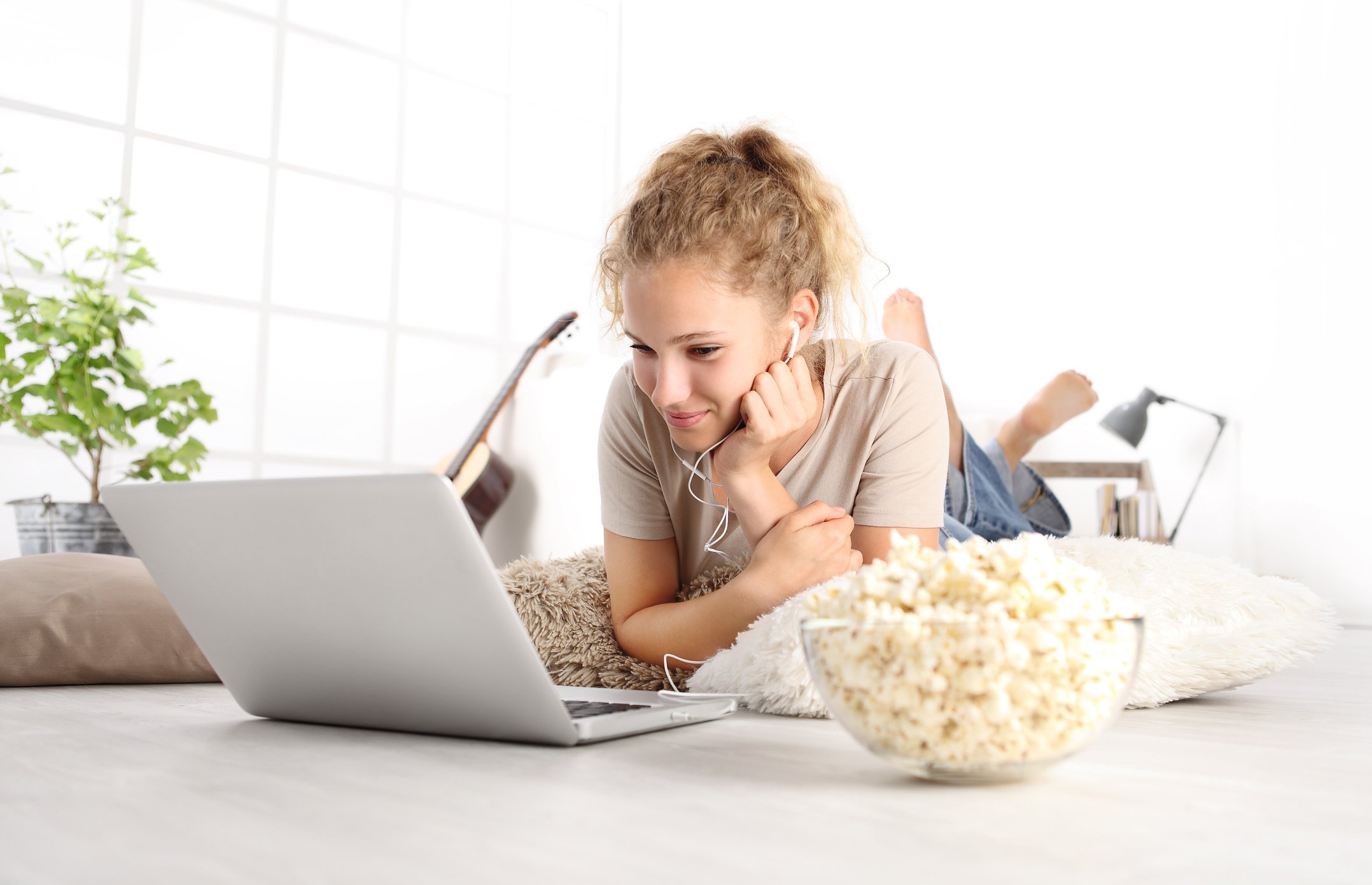 Girl watching a movie on her laptop with a bowl of popcorn nearby.