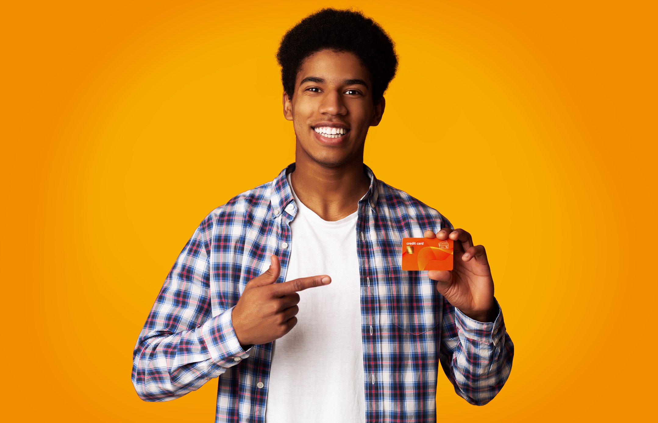 A young man points to a credit card in his other hand. 
