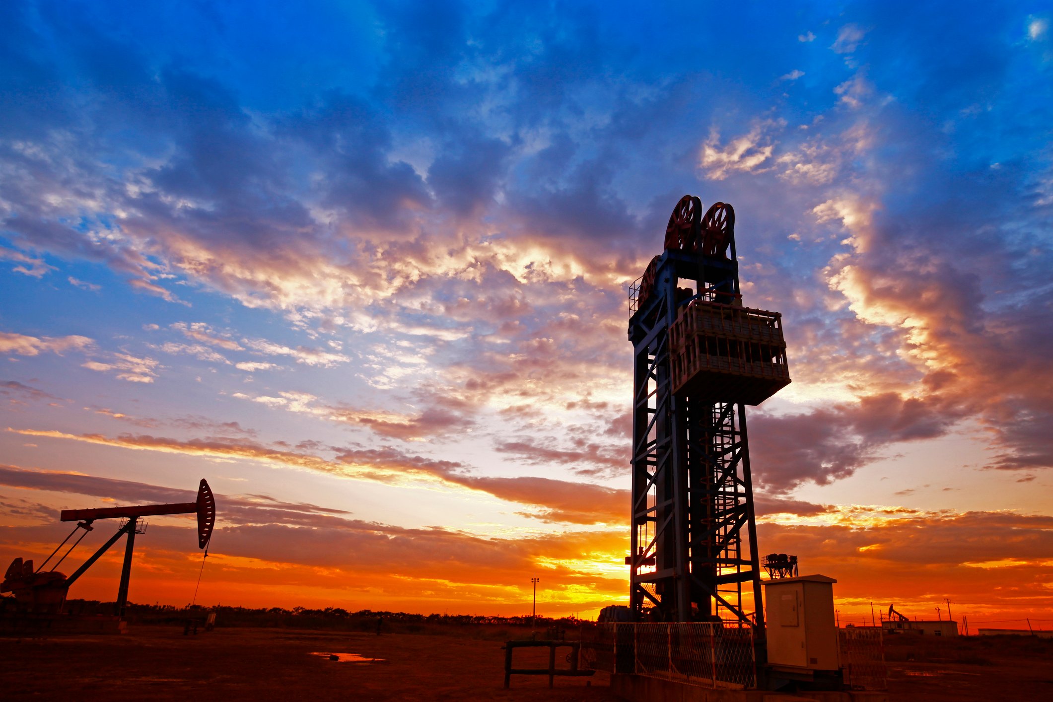 An oil drilling rig with the sun setting in the background.