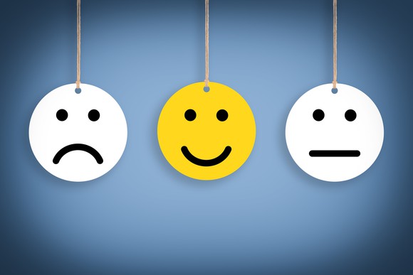 Yellow smiley face in between a white frowning face and a white stoic face