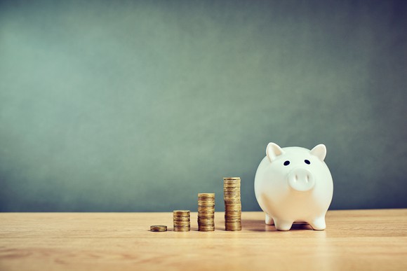 Piggybank and four stacks of growing coins on a table with a chalkboard in the background.