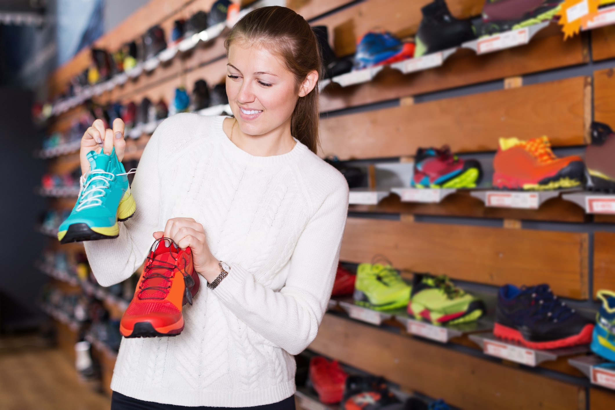 A woman holds up two different sneakers while shoe shopping