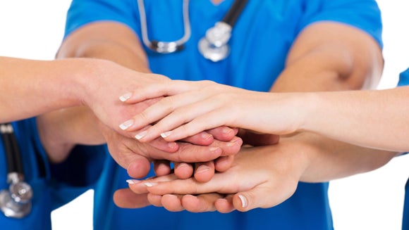 A team of people in medical gear does the thing where you stack hands atop each other like "Go team!"
