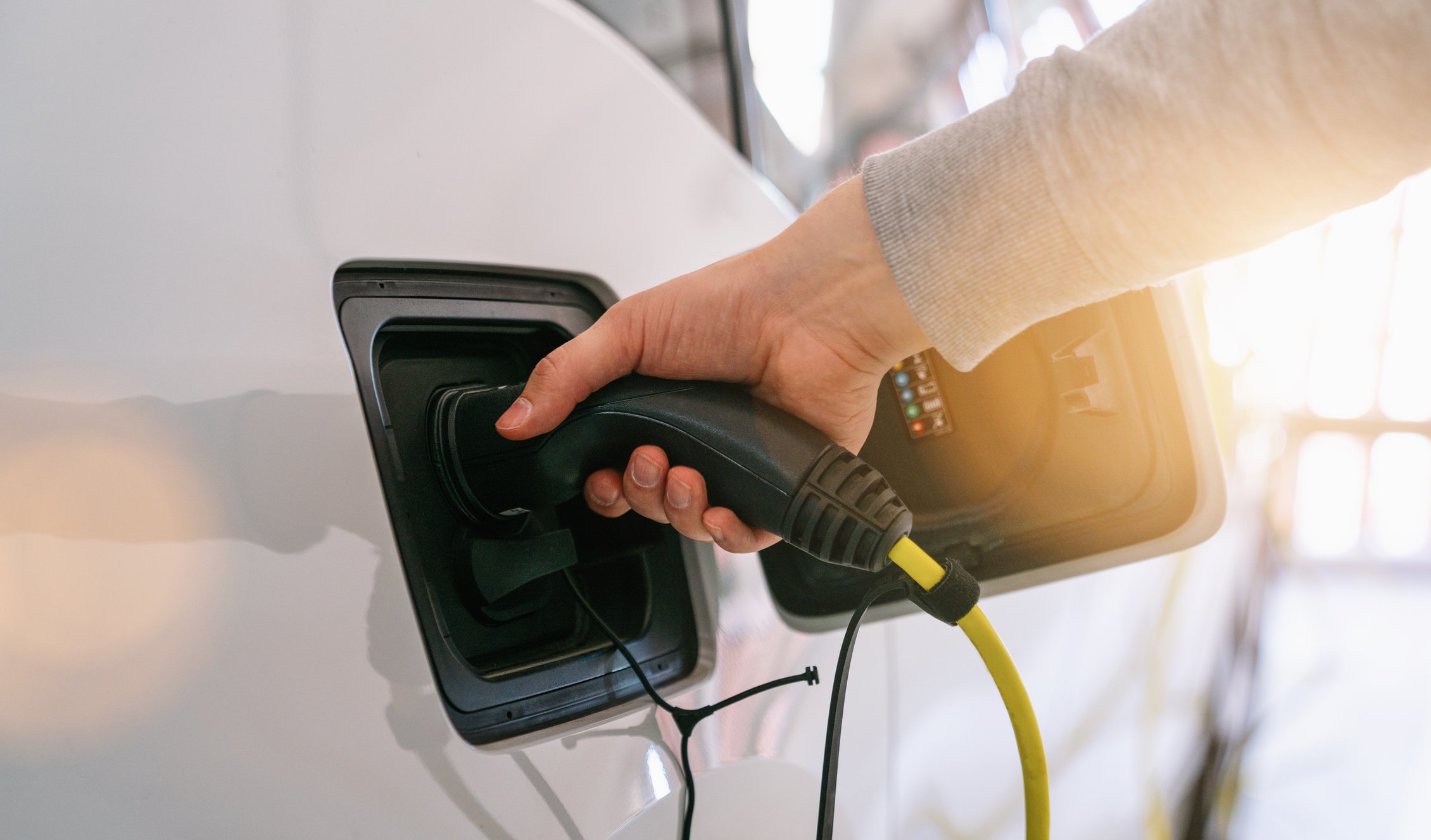 Man holding electric car charger plugged into car. 