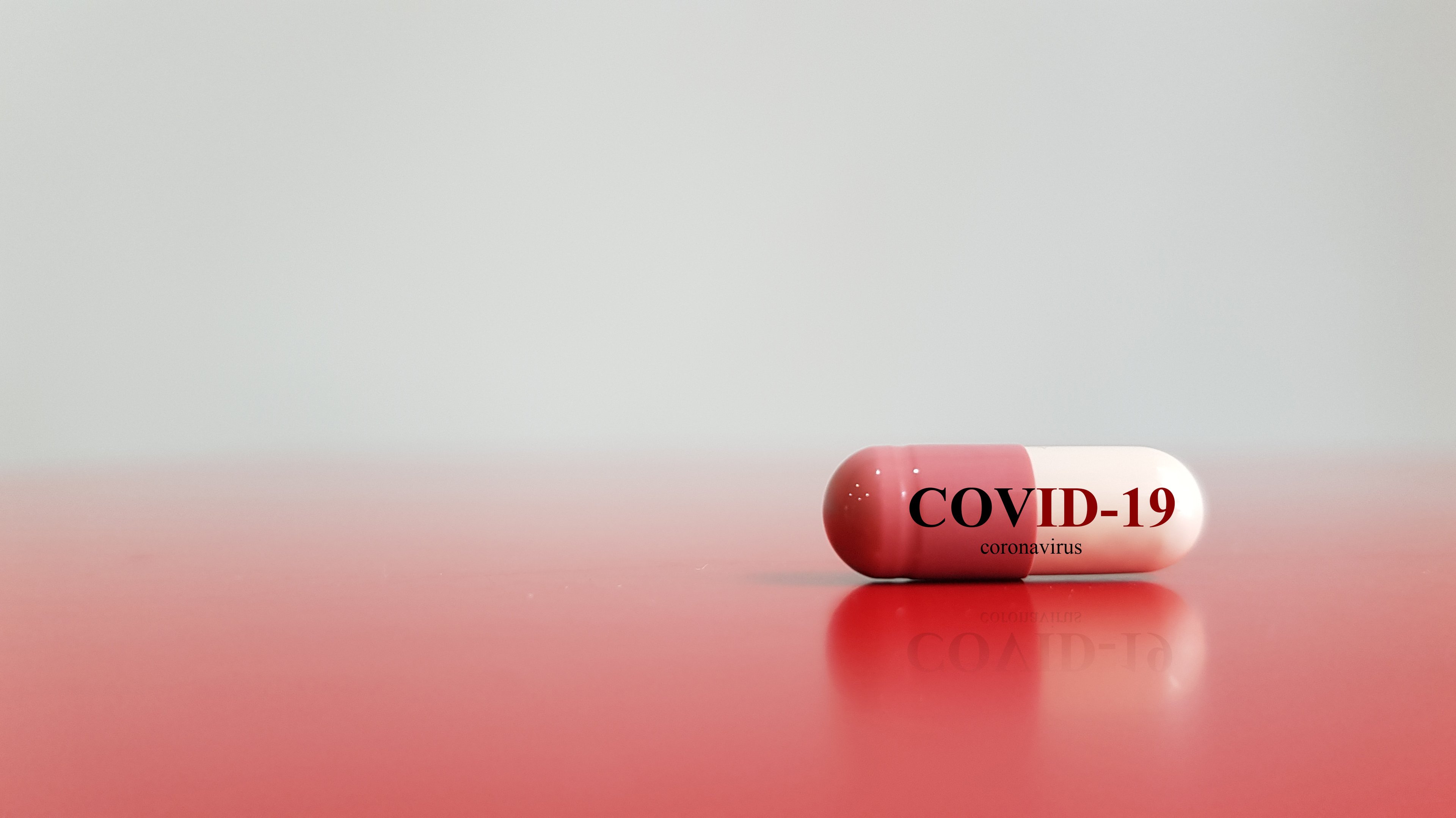 Red and white capsule with COVID-19 stamped on it sitting on red background.