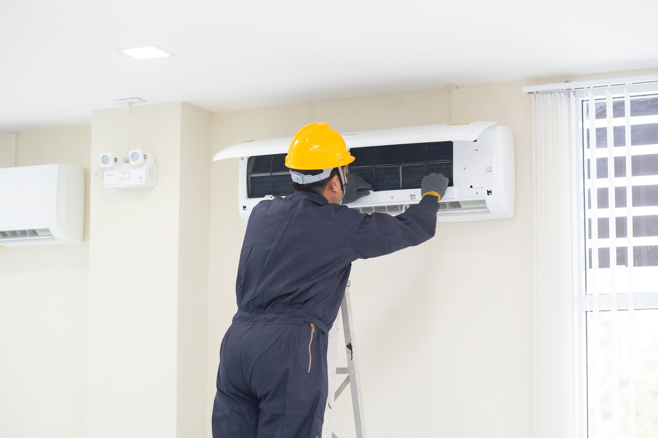 A man repairing a wall-mounted air conditioning unit.