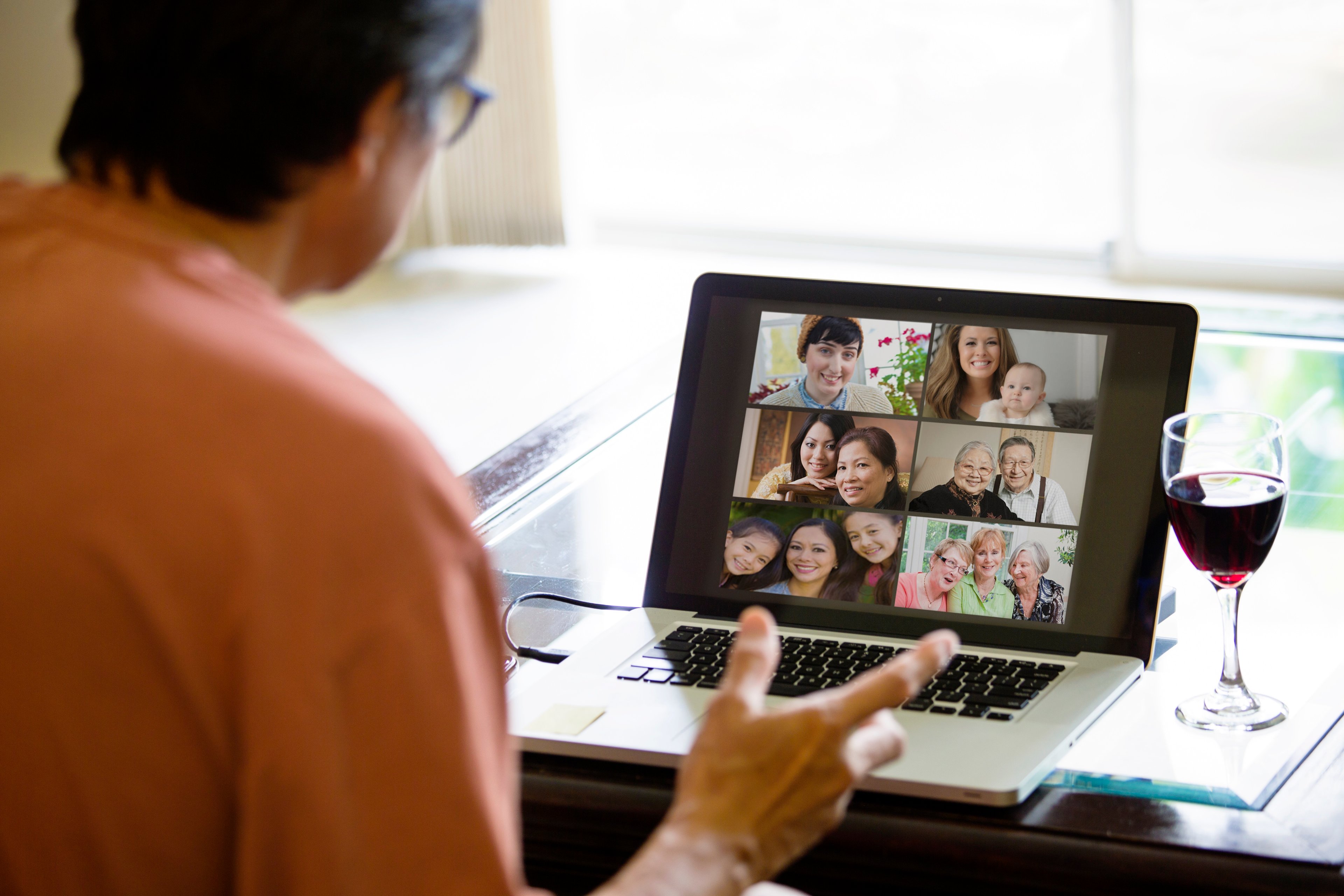 A man on a Zoom video call at his desk, with a glass of wine nearby.