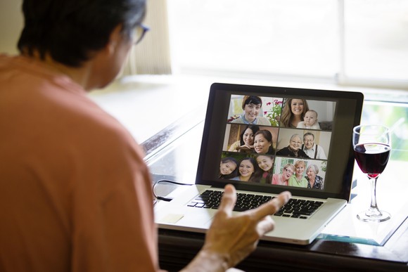 A man on a Zoom video call at his desk, with a glass of wine nearby.