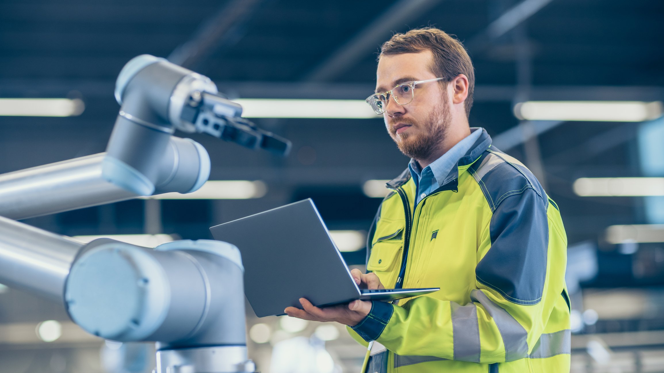 Man with a laptop programming a robotic arm.