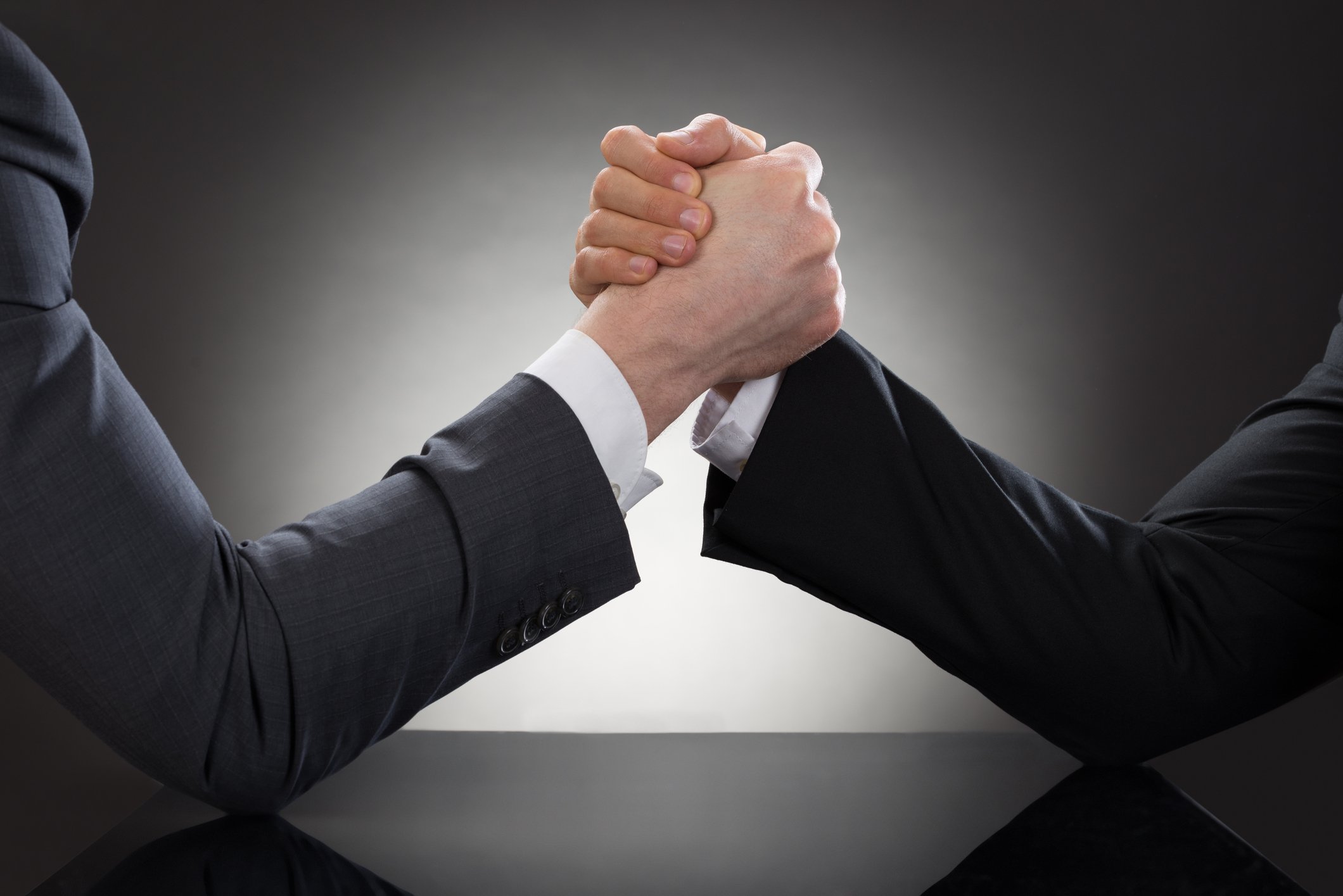Close-up photo of the hands of two businessmen engaged in arm wrestling.