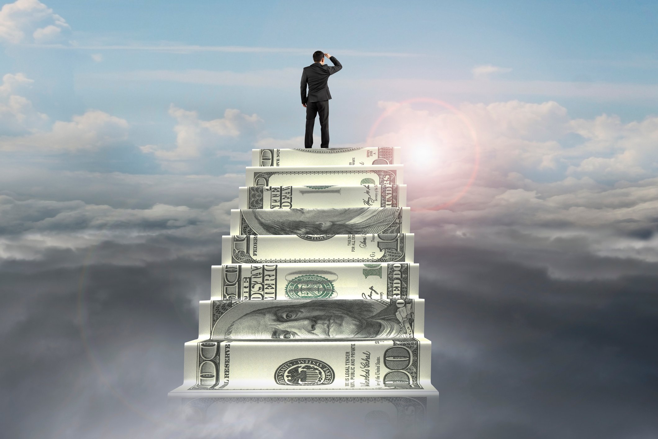 businessman on top of money stairs looking at sunlight 