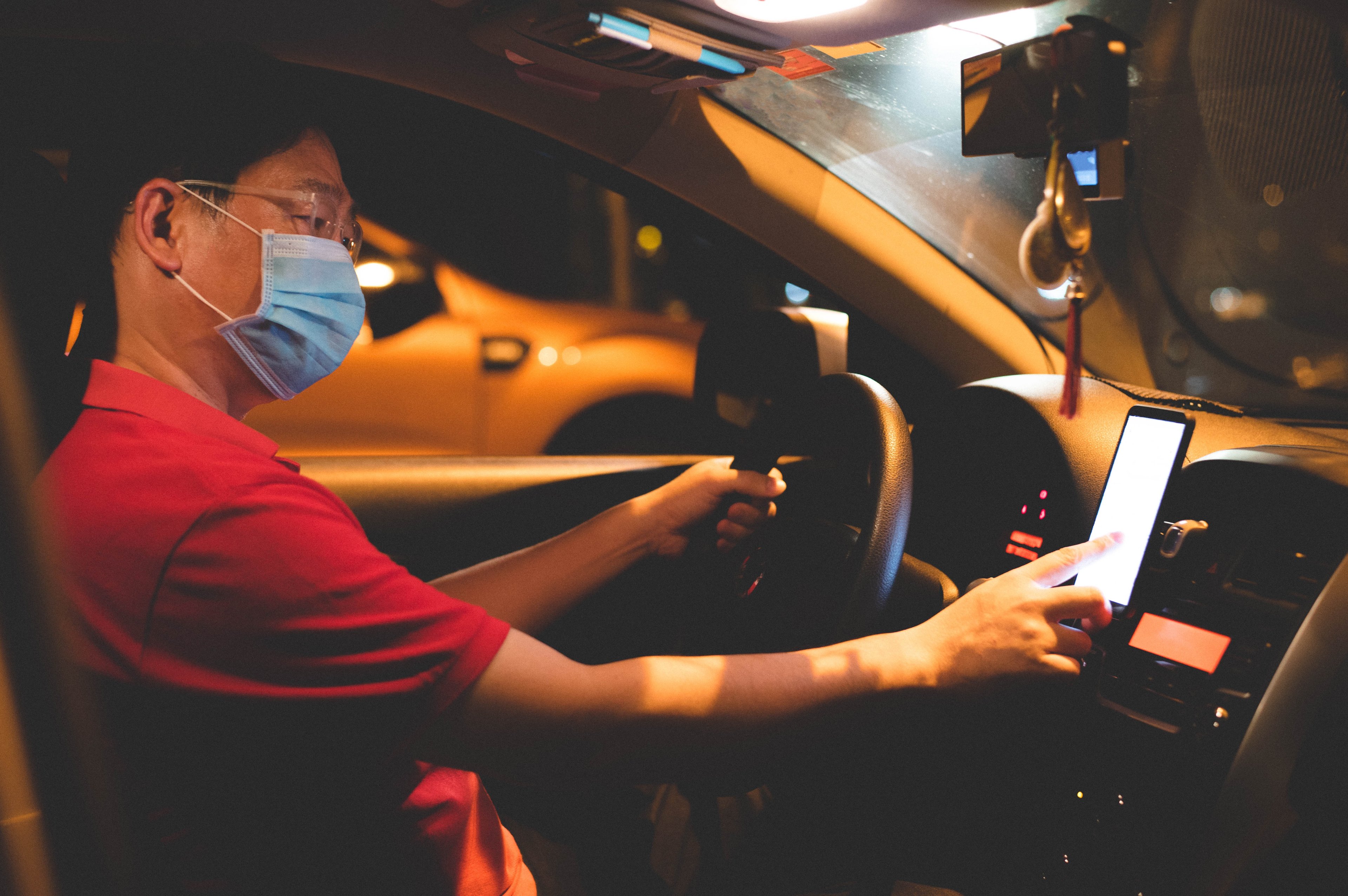 Ride-hailing driver wearing a mask and looking at a GPS map in his car. 