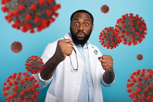 A medic lifts his hands to punch at several exaggerated coronavirus particles floating in the air.