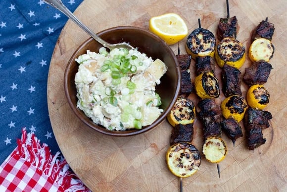 A Blue Apron meal of steak and squash kebabs with potato salad on a cutting board