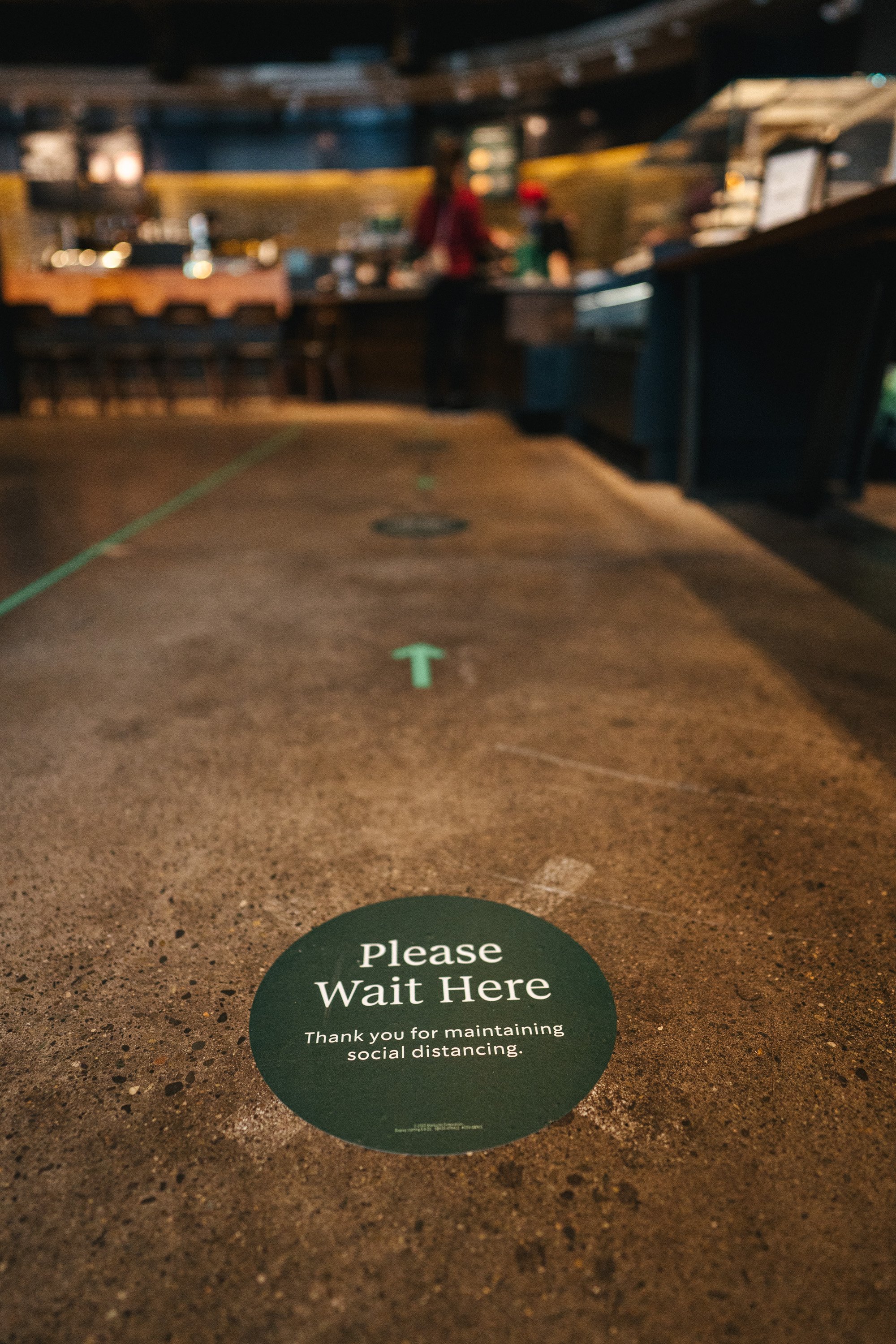 An entrance to a Starbucks shop is shown, with a sign saying "Please wait here."