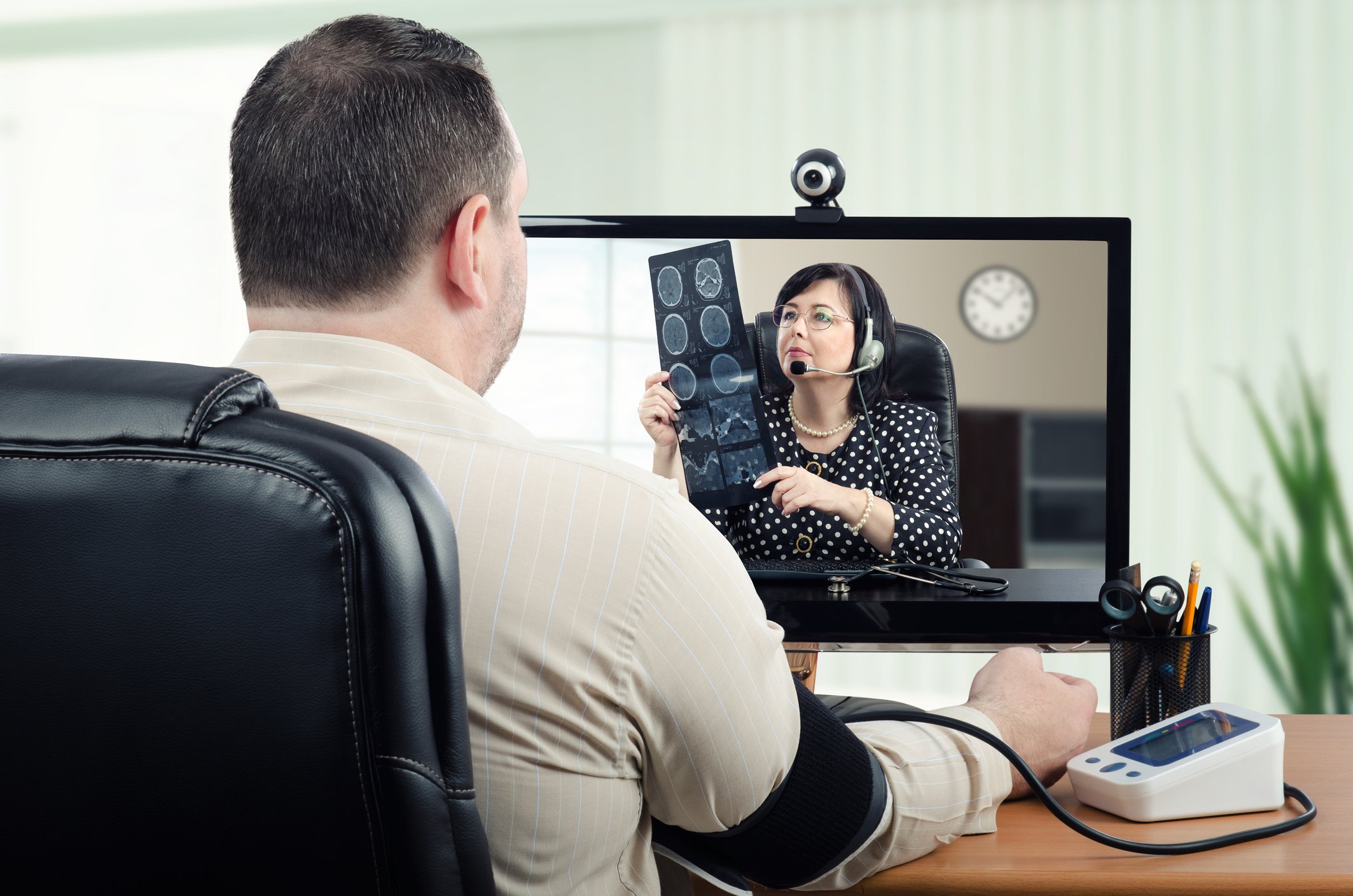 A person is hooked up to a blood pressure measuring device while having a video conference with a doctor.