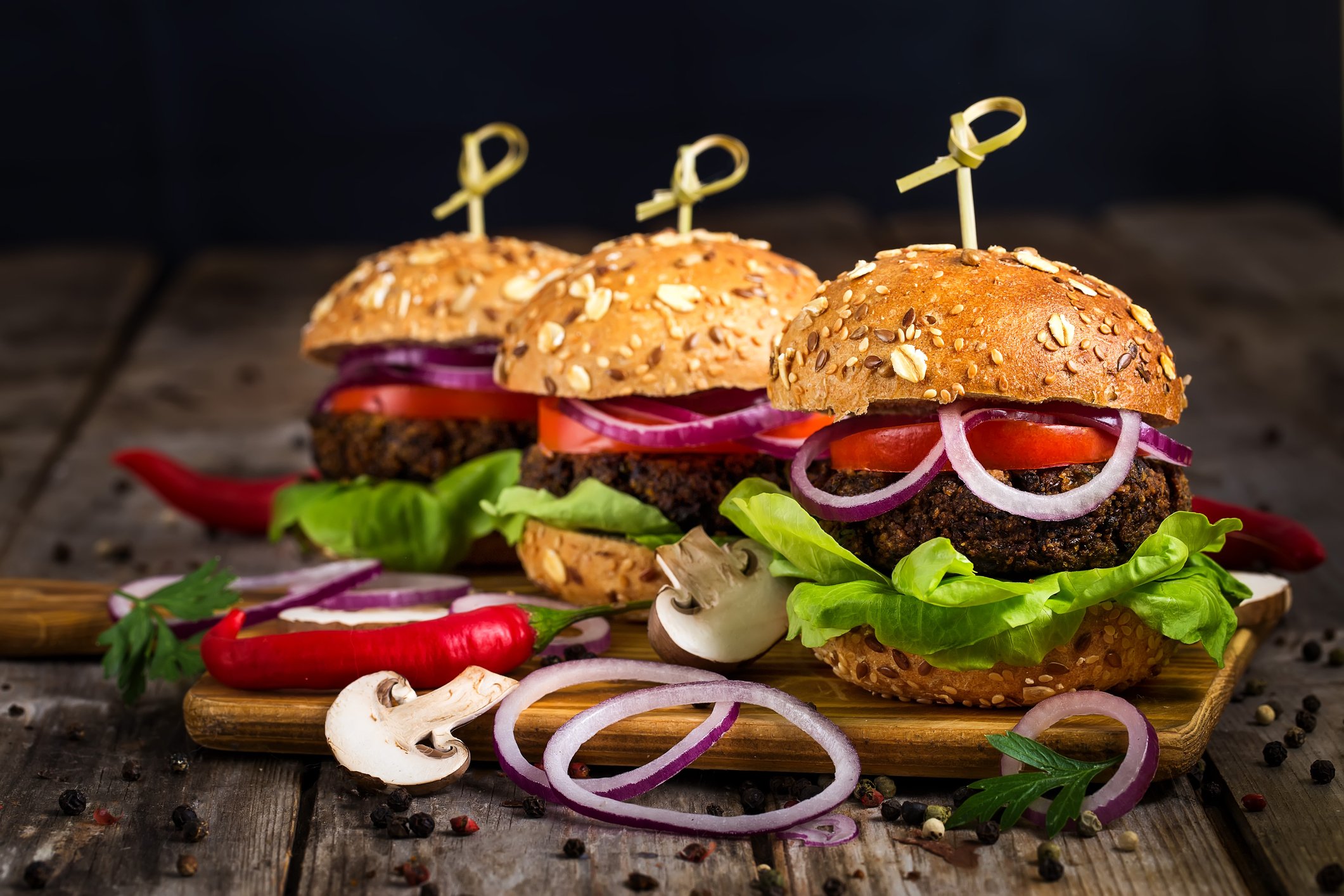 Three veggie burgers, overflowing with lettuce and onions, sit on a wooden surface.