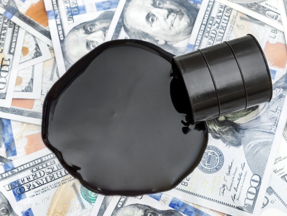 An oil drum spills black liquid onto $100 bills.