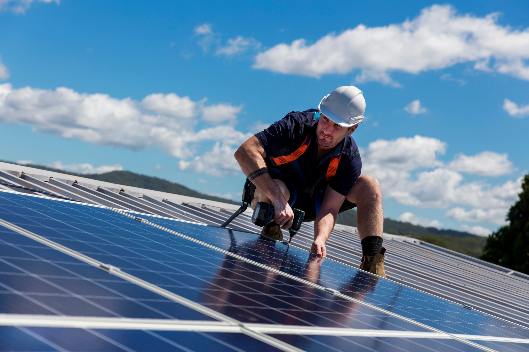 A solar panel installer works with a drill on a roof.