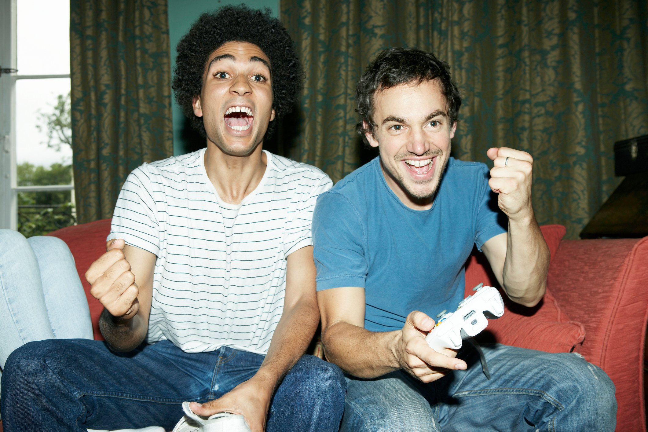 Two young men pump fists in victory at the  TV while playing video games. 