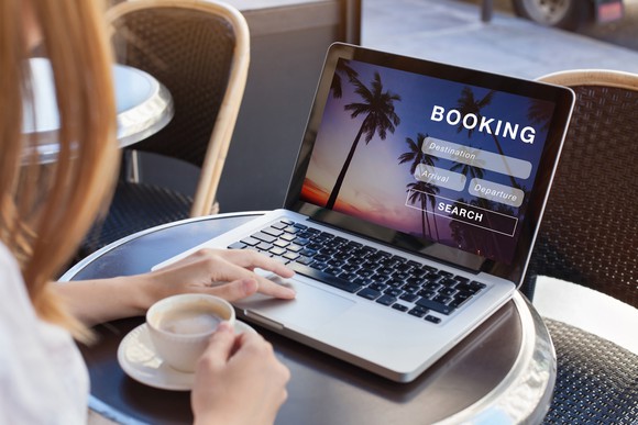 A person sitting at a table with an open laptop showing the word Booking on the screen.