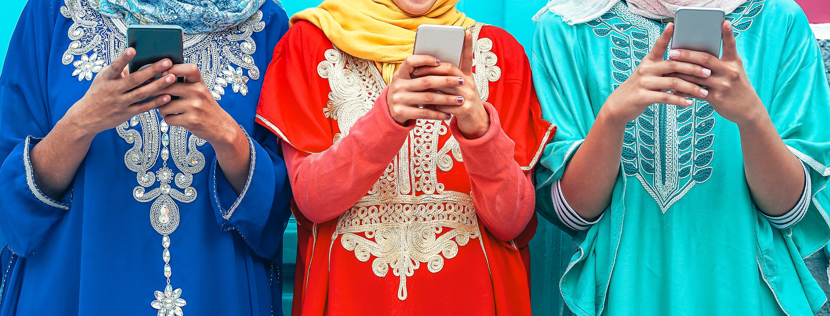 Three Indian women stand in a row, all holding up smartphones