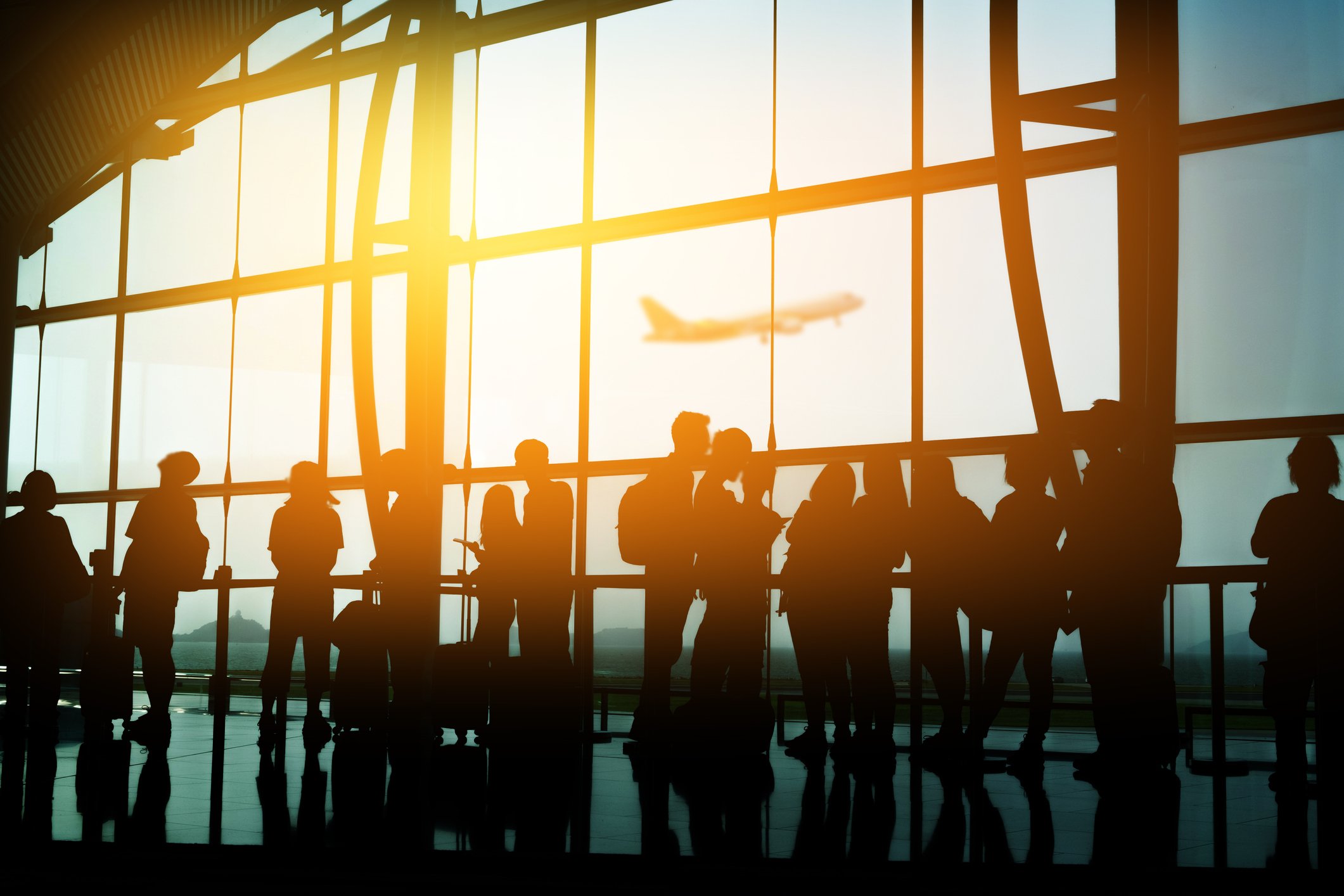 Passengers in silhouette standing in line at an airport terminal.