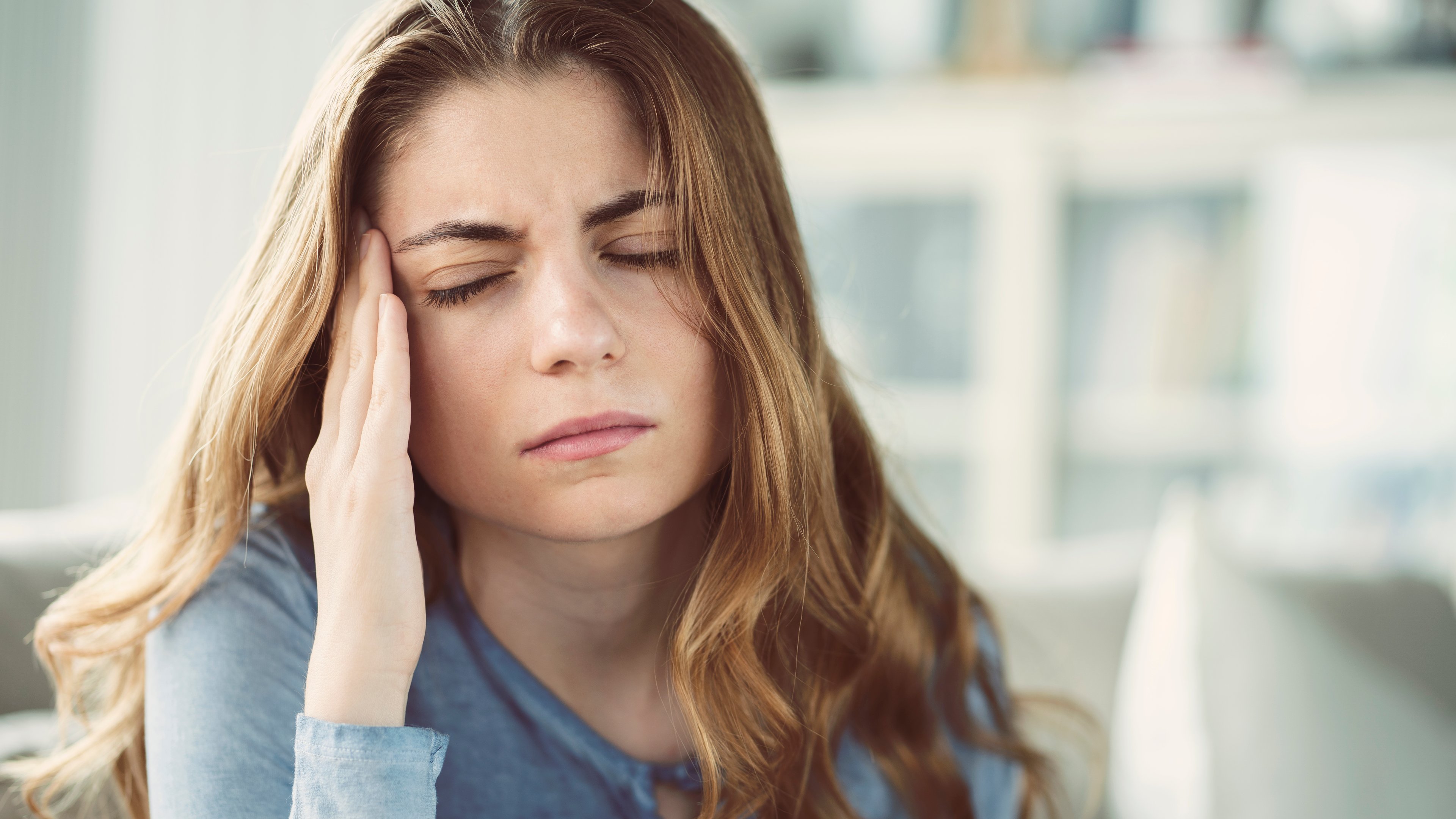 Young woman with headache in home interior.