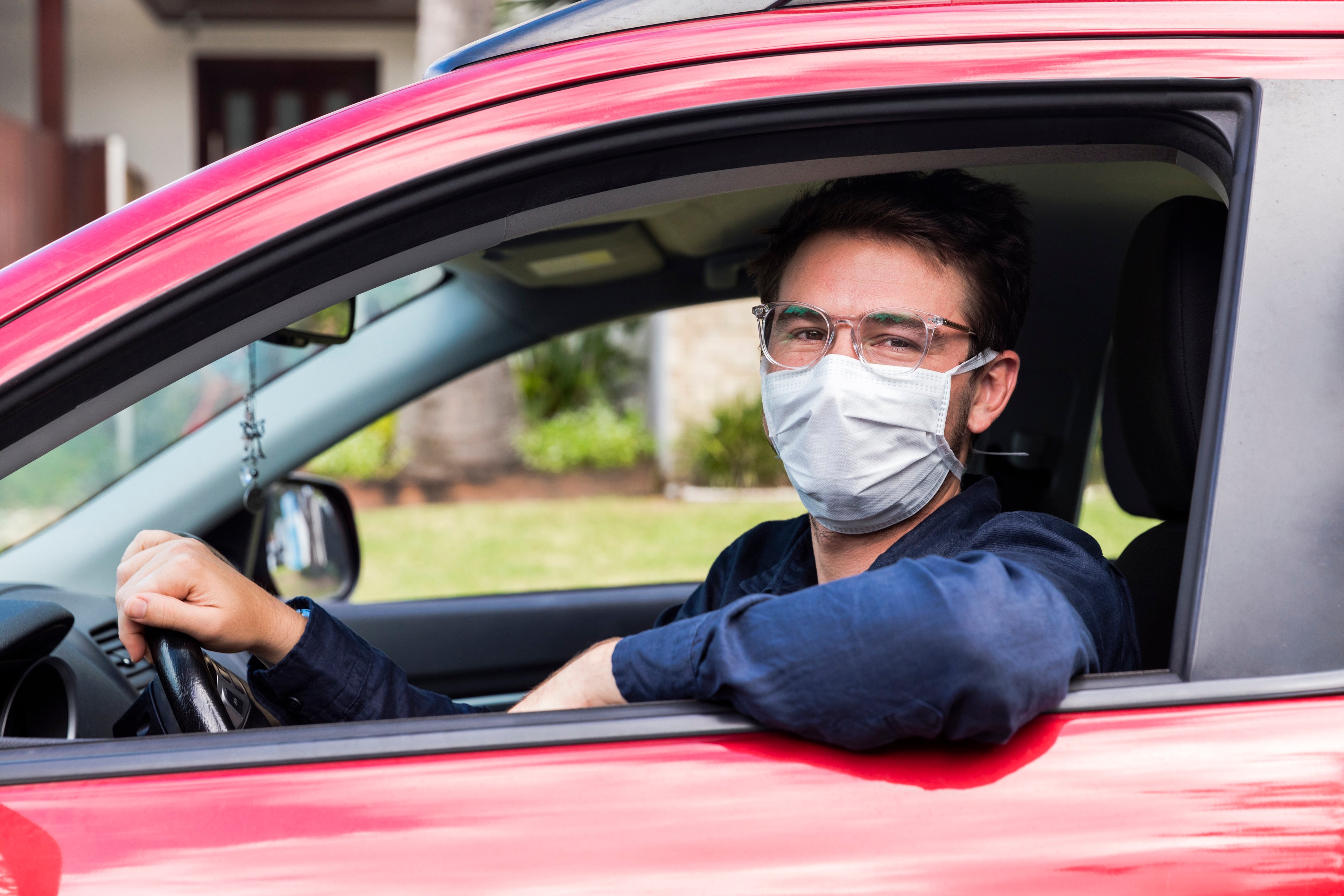 A ride-hailing driver in a red car wearing a face mask. 