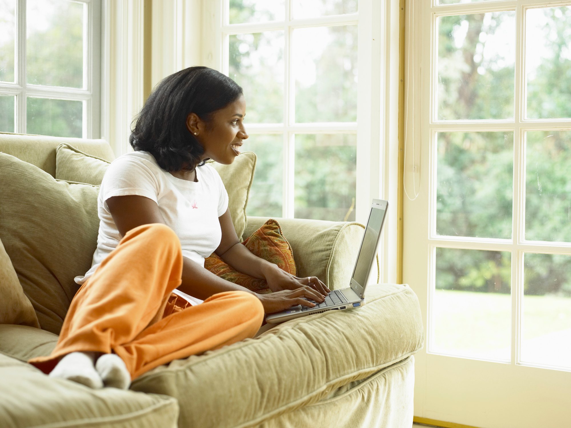 A young woman lounging on a sofa in comfortable clothes and using a laptop computer.