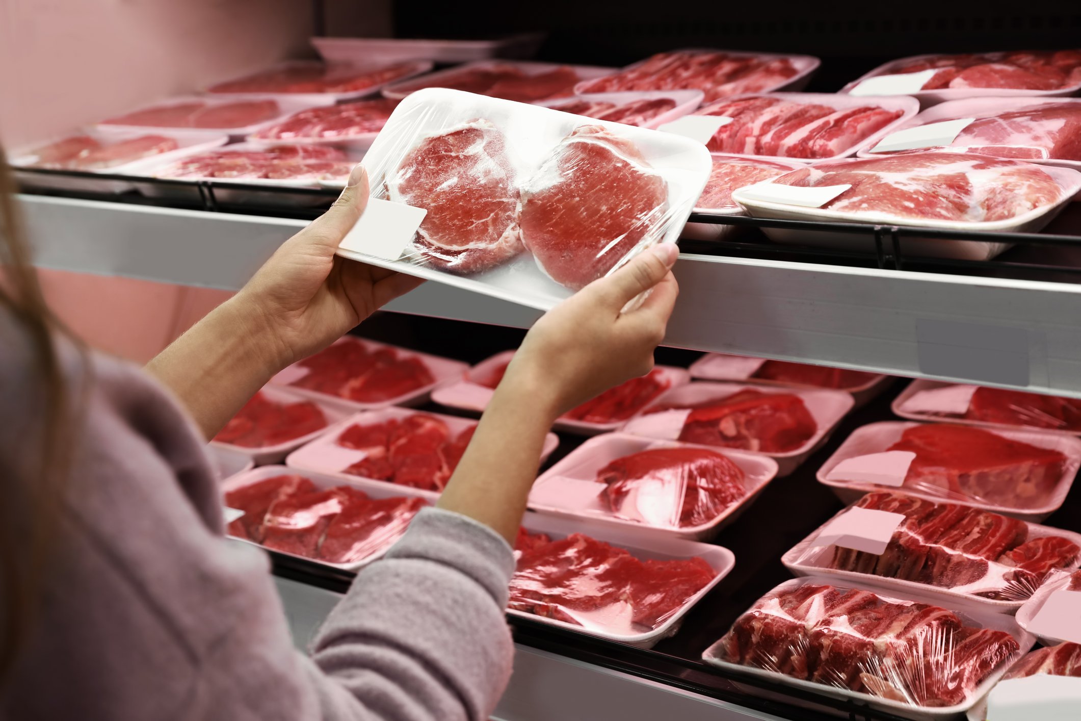 A shopper examines cuts of meat at a grocery store.