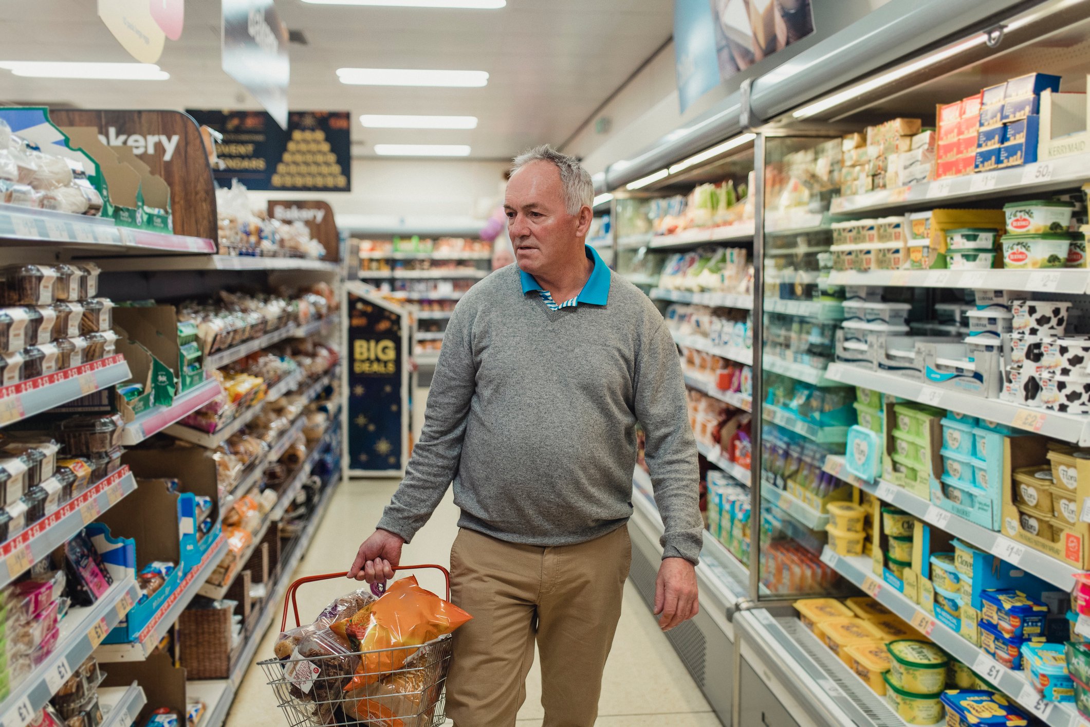 Senior citizen carrying basket while shopping for groceries.