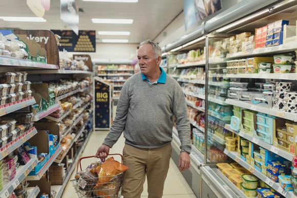 Senior citizen carrying basket while shopping for groceries.