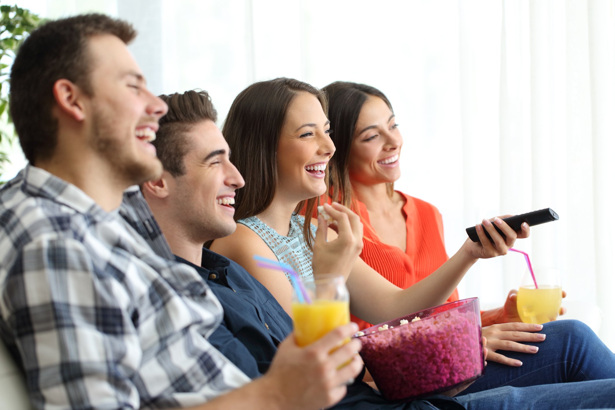 A group of our young friends share drinks and popcorn on a couch, lauching at the unseen TV.