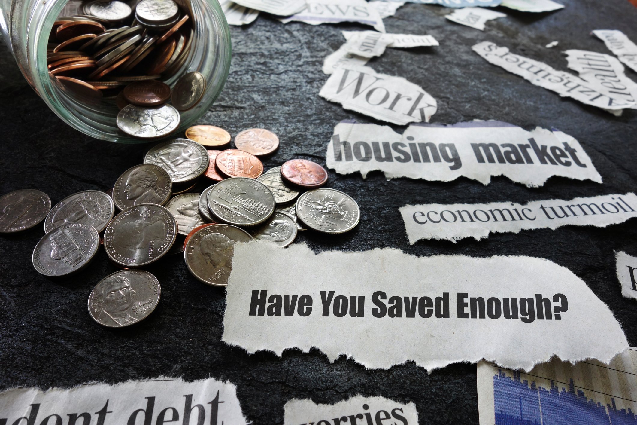 A jar of coins spilled on a table with various notes on it that say Have You Saved Enough? and economic turmoil, among others.