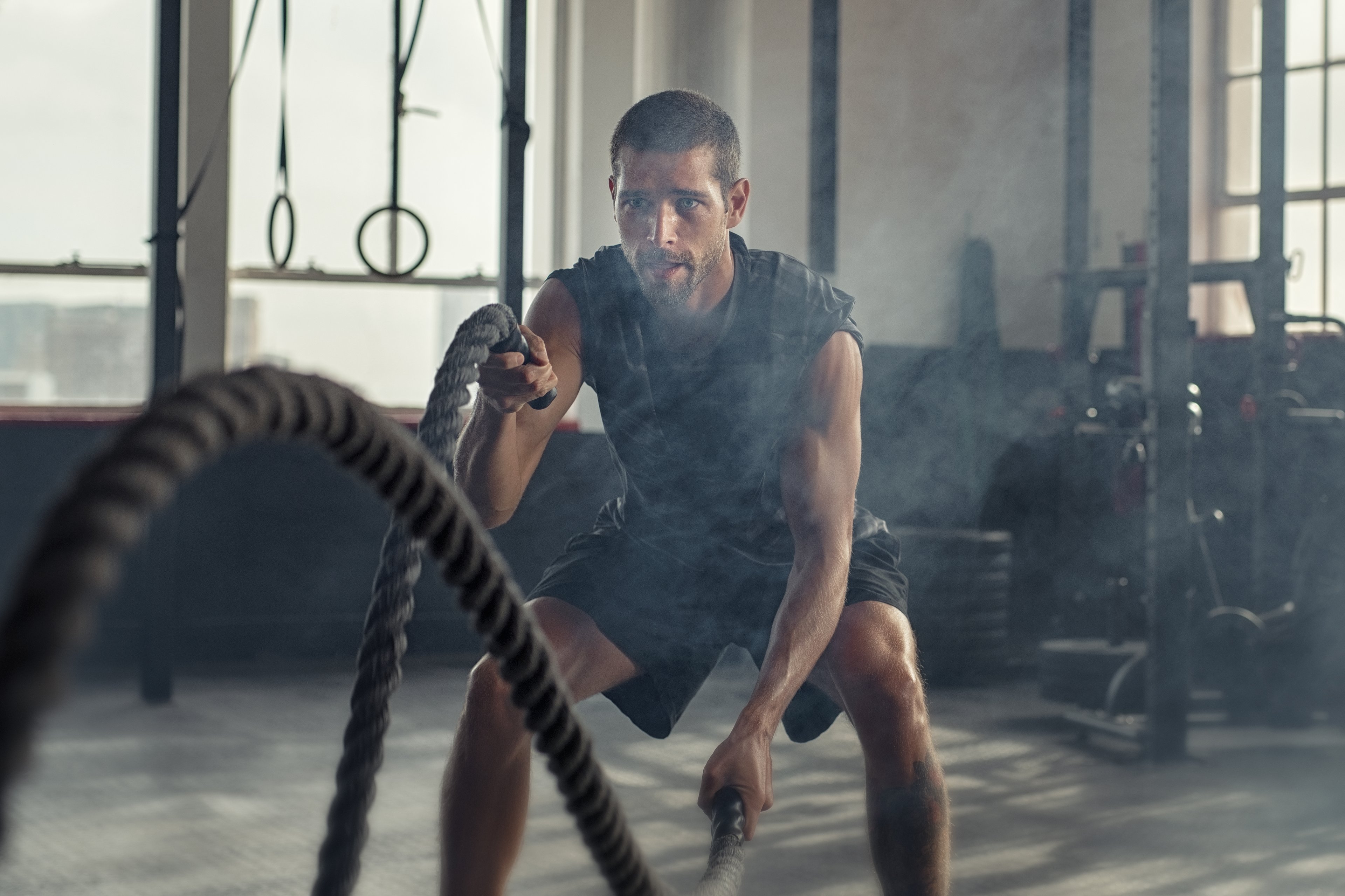 Young man in gym exercising with ropes.