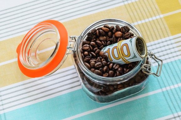 A roll of hundred-dollar bills sticking out of a glass jar full of coffee beans.