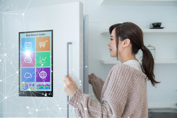 A woman opening a refrigerator with a digital screen on the door and illustration showing internet connectivity.