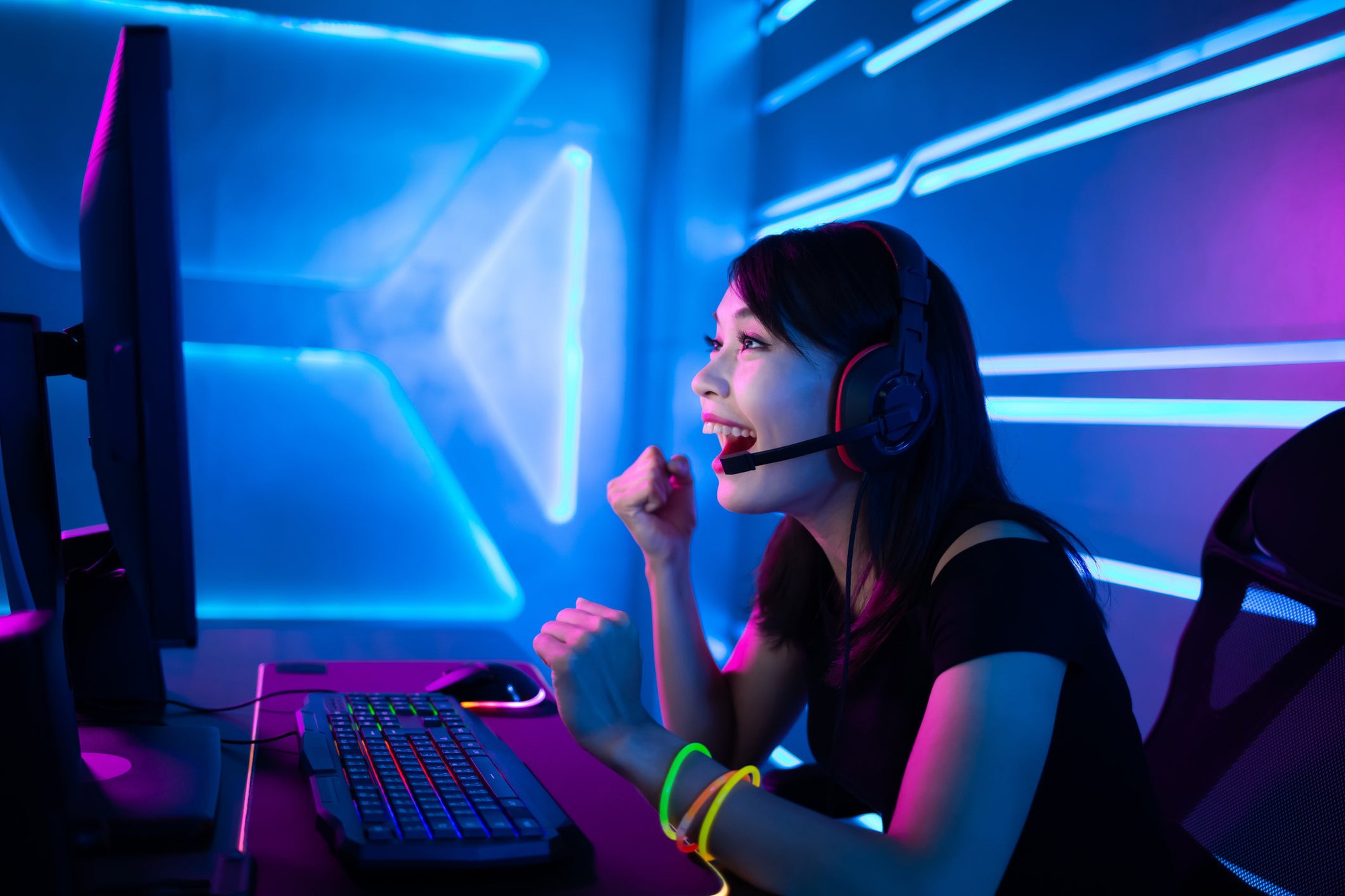 A woman watching something exciting on a large screen PC monitor. She's wearing a headset and glowing bracelets.