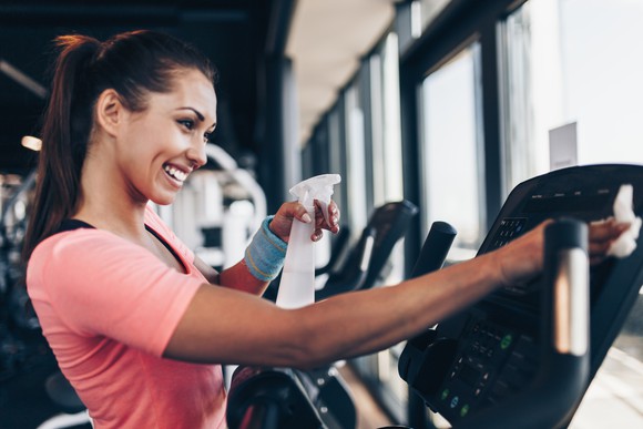 Young woman cleaning off gym equipment.
