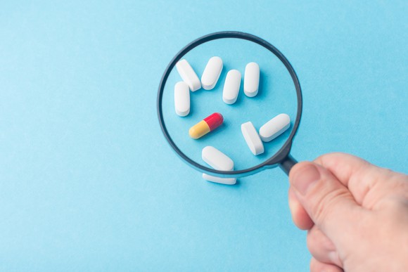 White pills and one red and yellow capsule seen through a magnifying glass.
