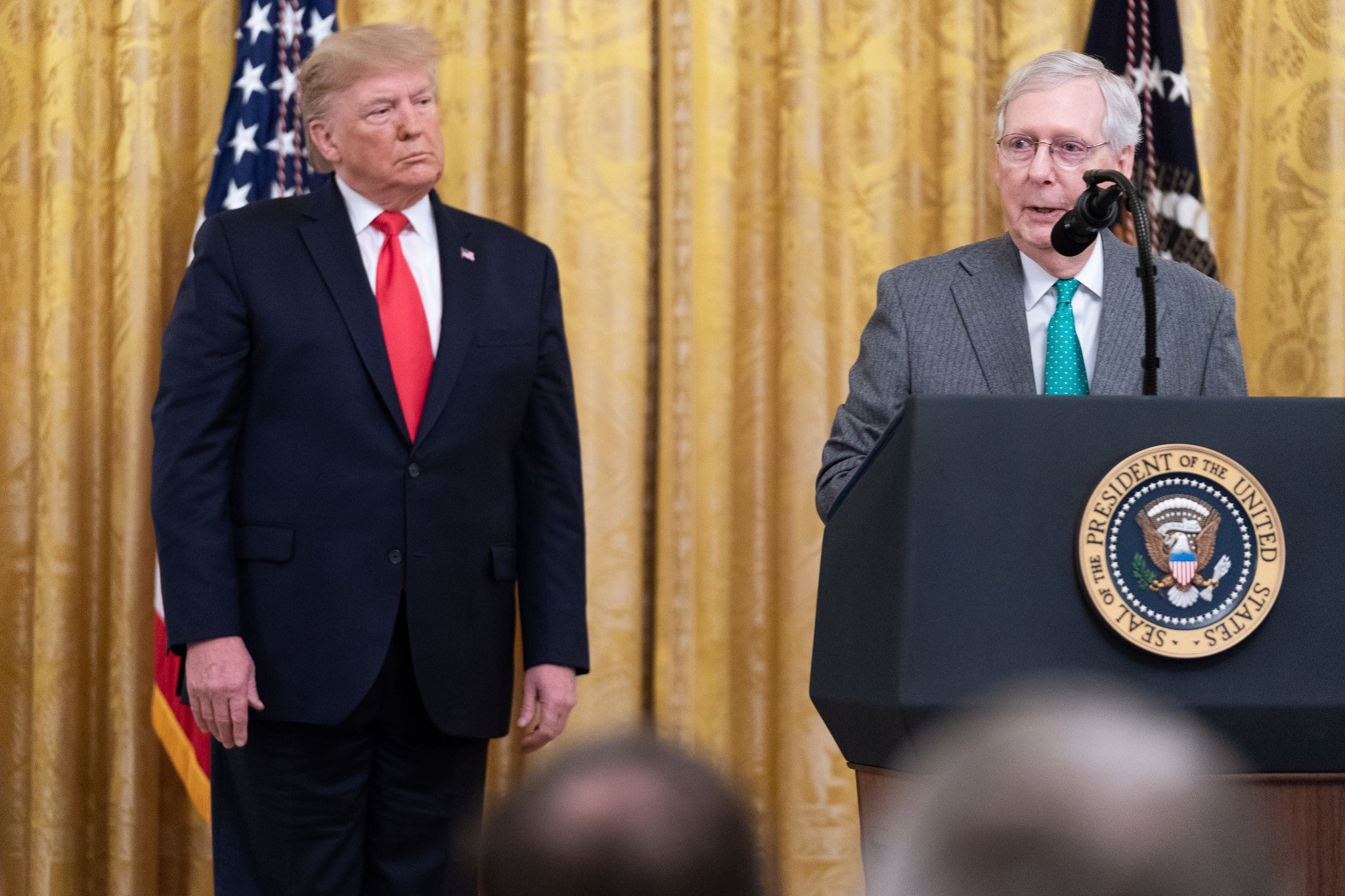 Senate Majority Leader Mitch McConnell speaking to reporters, while flanked by President Trump.