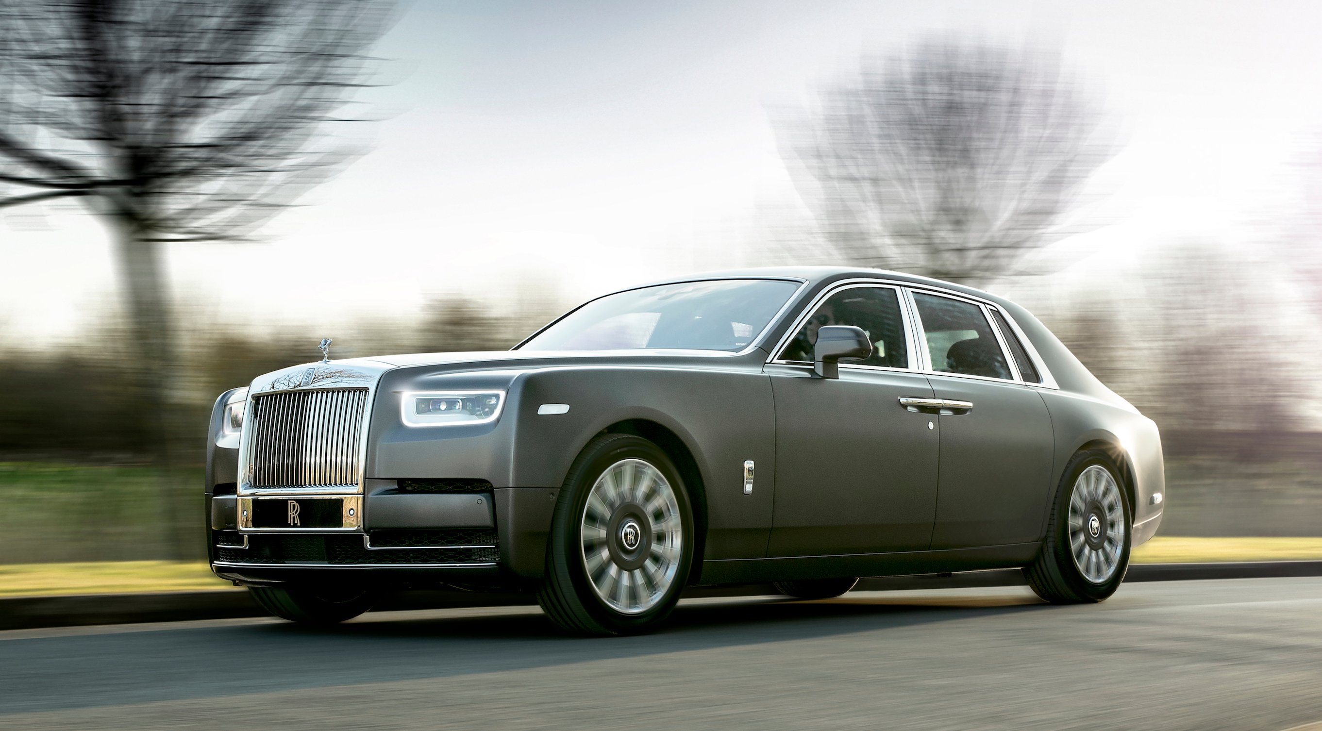 A gray Rolls-Royce Phantom, a large ultra-luxury sedan, on a country road