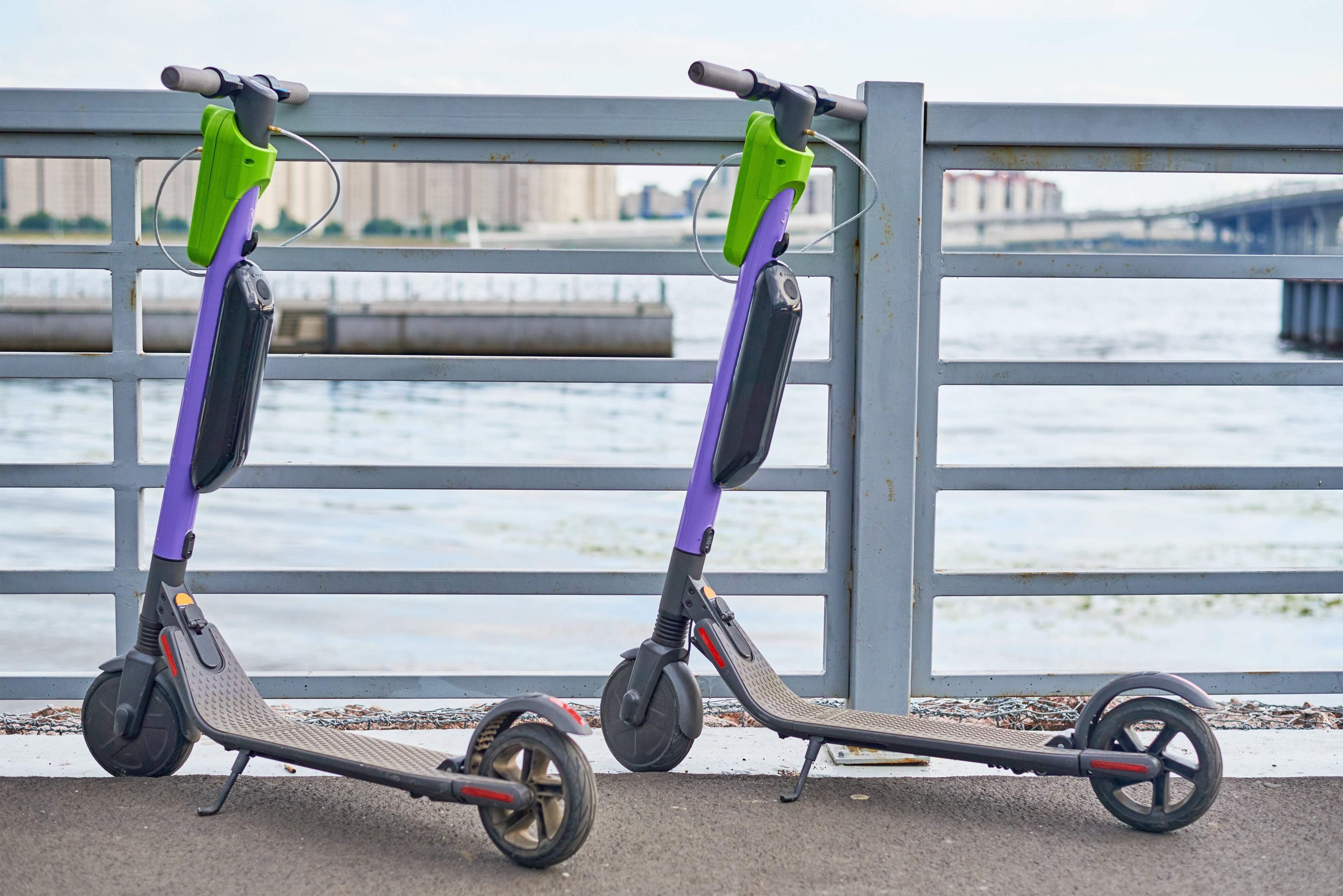 Two electric scooters parked, facing the river in a city. 