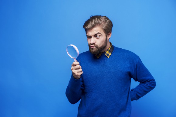 A bearded man looks through a magnifying glass.