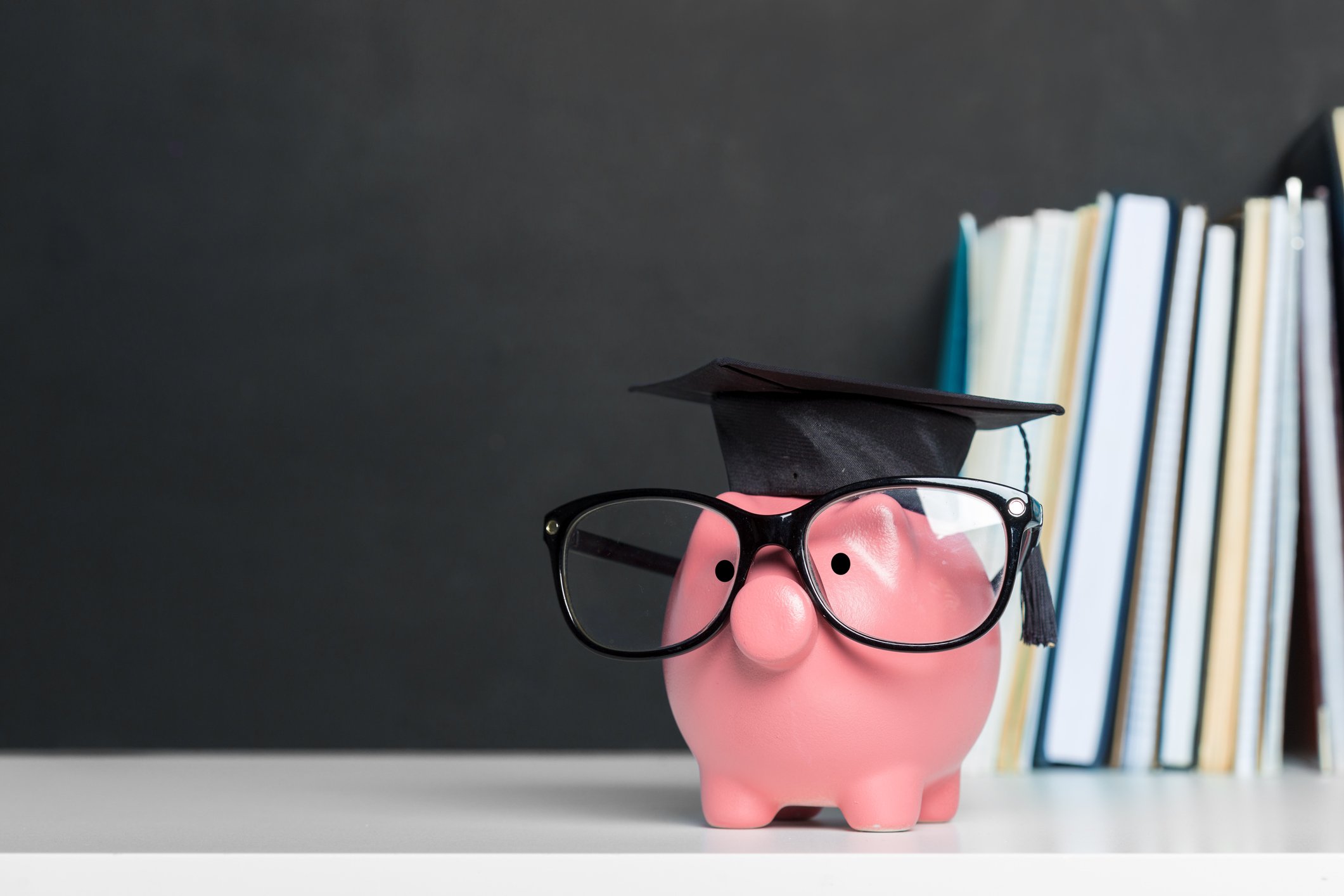 Piggy bank dressed with glasses and a mortarboard hat and books in the background.