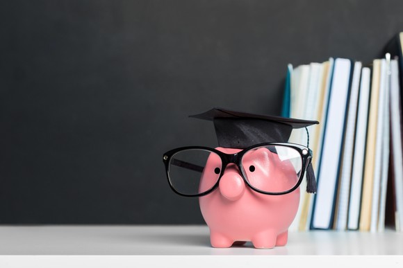 Piggy bank dressed with glasses and a mortarboard hat and books in the background.