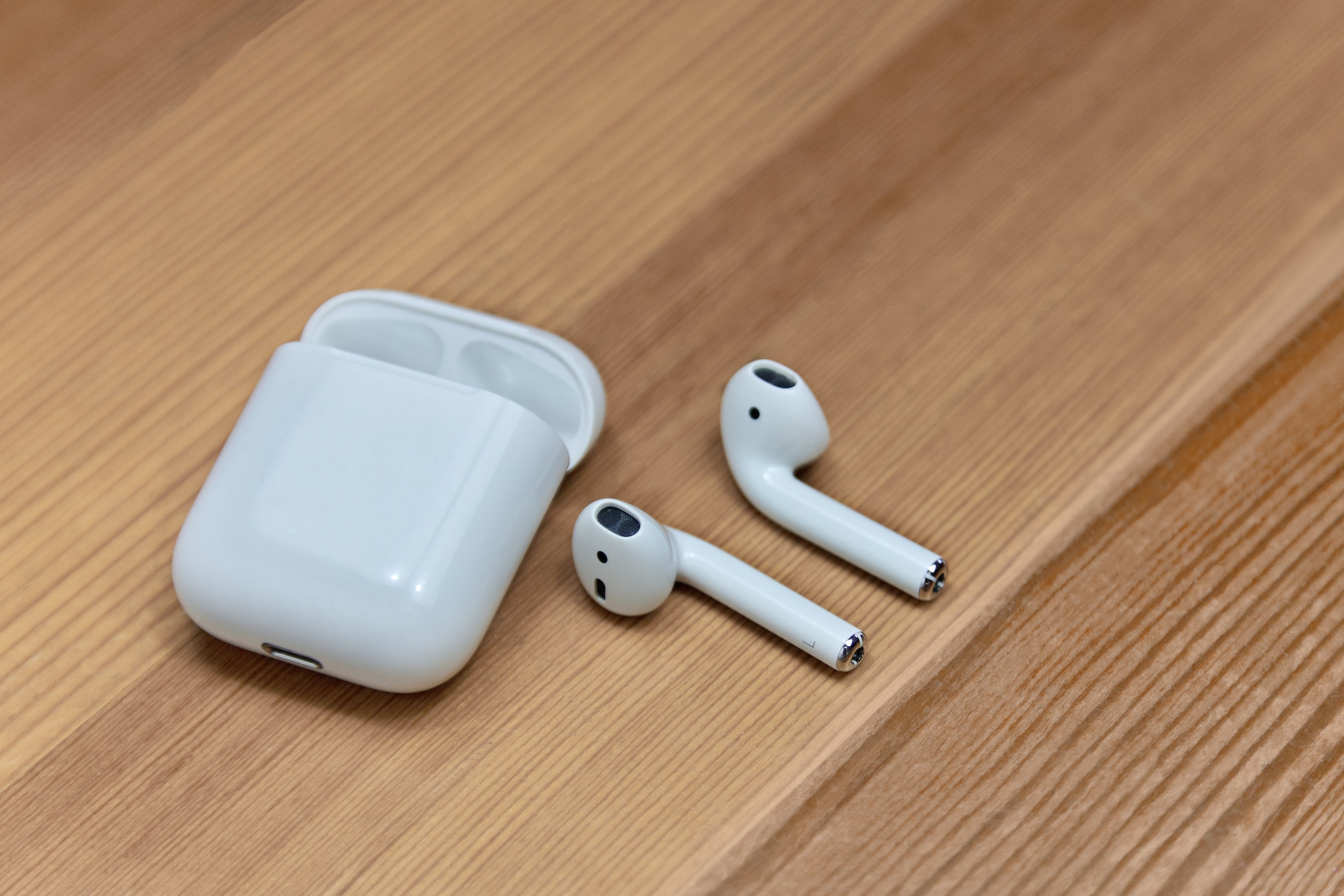Apple AirPods and charging case sitting on a wood table. 